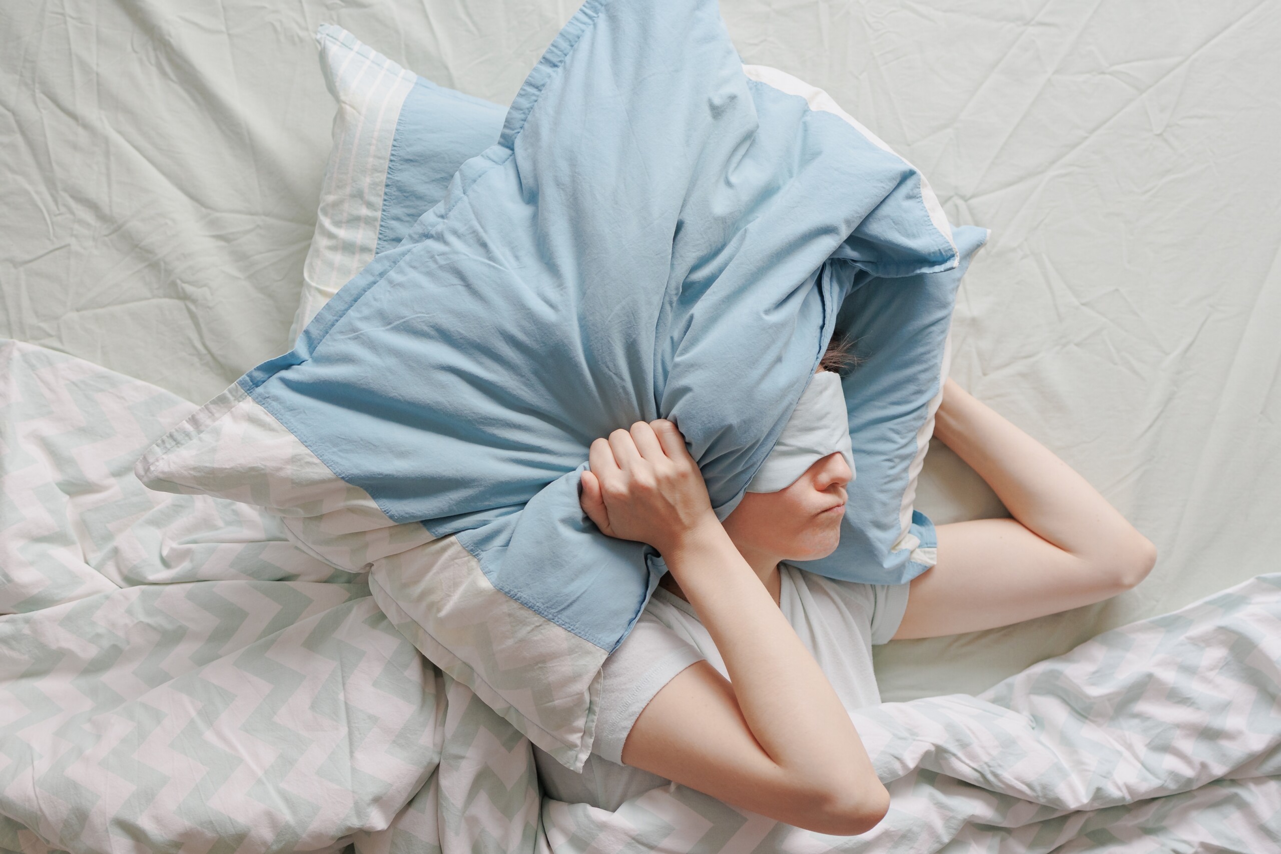 Woman with insomnia covering her head with a pillow, unable to fall asleep.